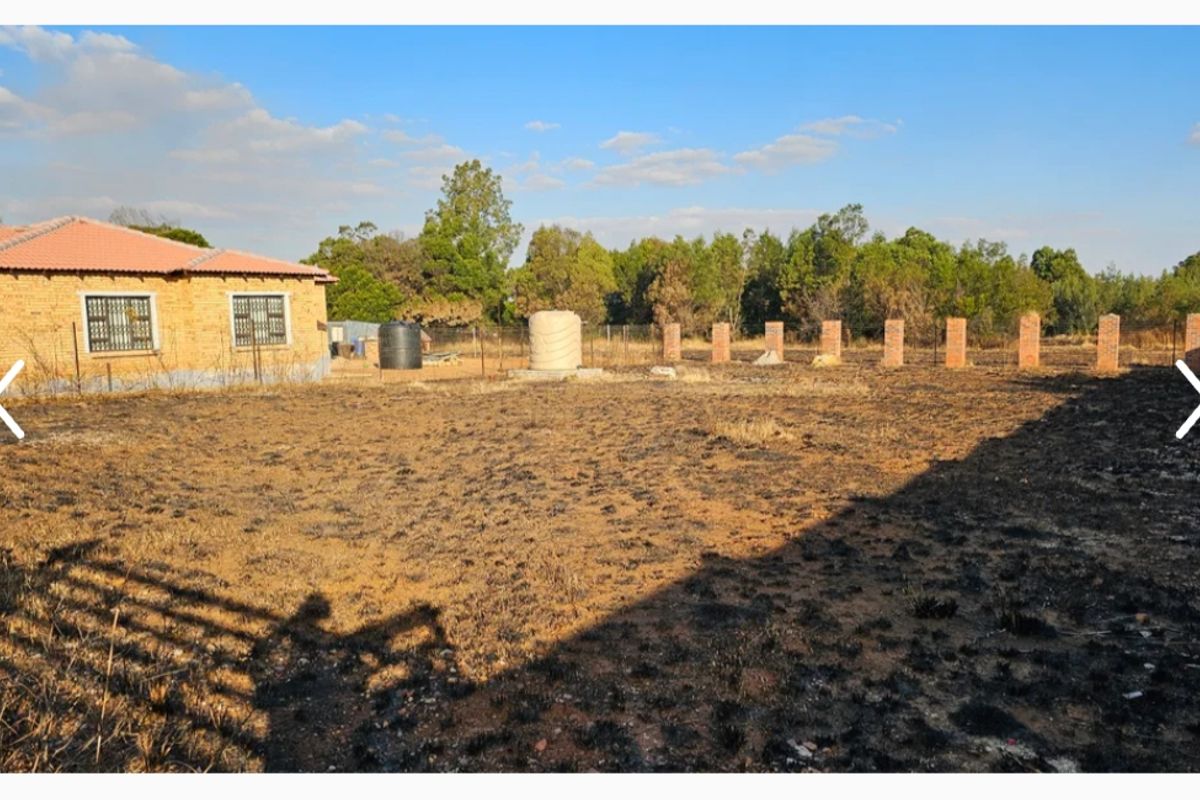 A view of the rear yard featuring a brick perimeter fence, water storage tank, and a residential structure with a tiled roof.