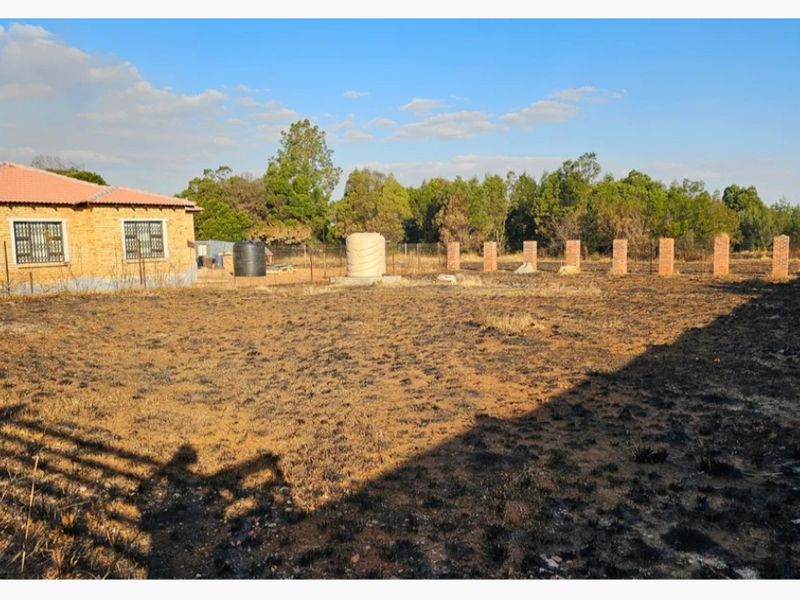 A view of the rear yard featuring a brick perimeter fence, water storage tank, and a residential structure with a tiled roof.