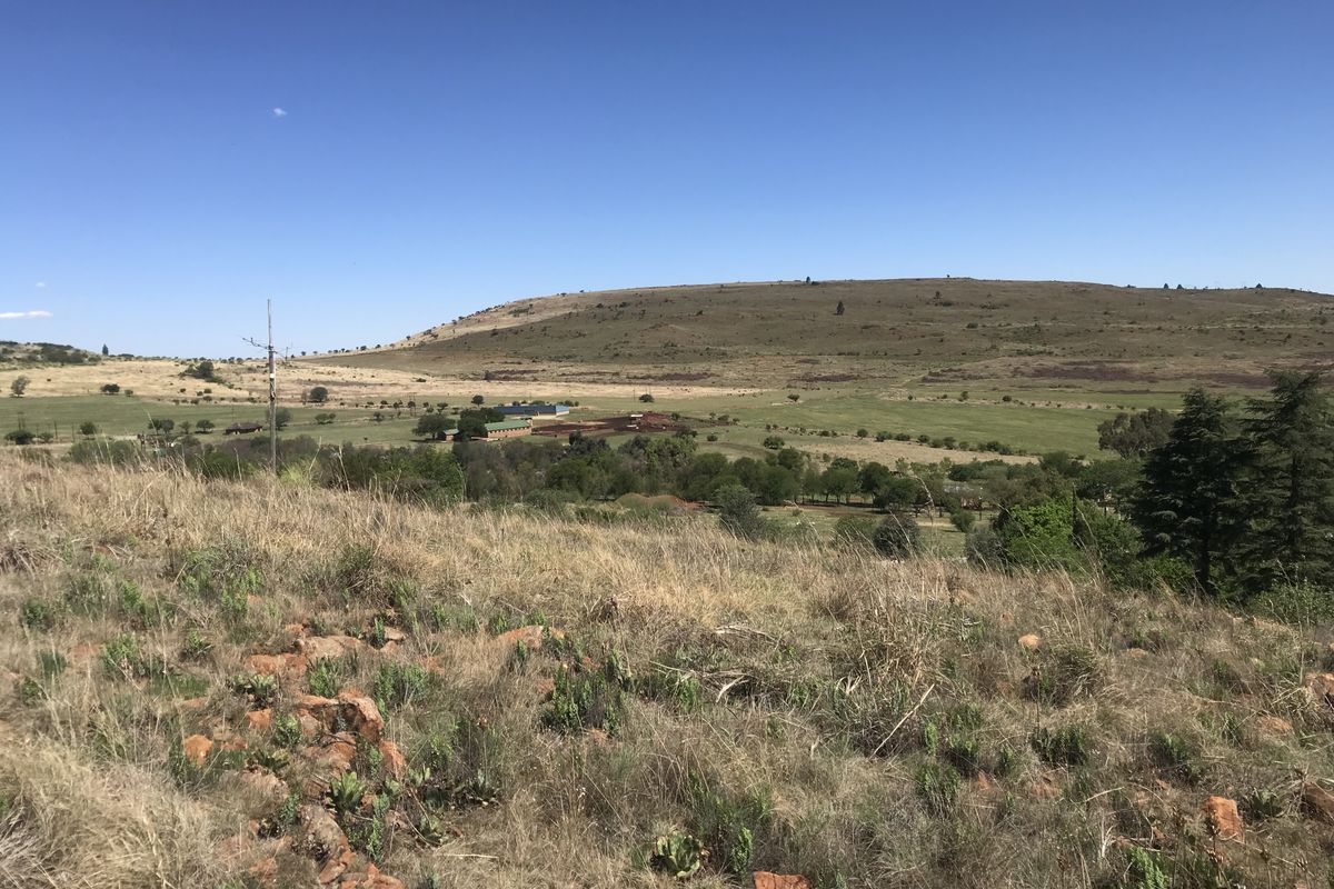 A wide-angle view of the expansive vacant residential land, featuring rolling hills, natural vegetation, and distant rural structures under a clear blue sky.