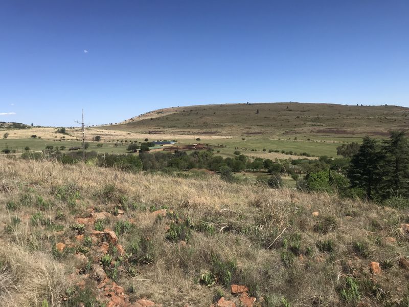 A wide-angle view of the expansive vacant residential land, featuring rolling hills, natural vegetation, and distant rural structures under a clear blue sky.