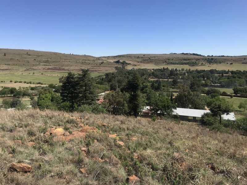 A scenic elevated view overlooking a rural landscape with rolling hills, natural vegetation, and distant residential structures.