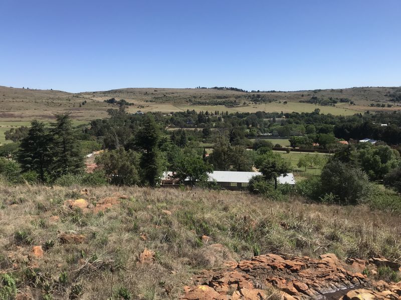 A scenic elevated view overlooking a rural landscape with rolling hills, natural vegetation, and distant residential structures.