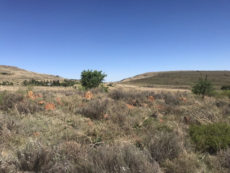 A wide-angle view of the vacant residential land featuring natural rocky terrain and open landscape under a clear blue sky.