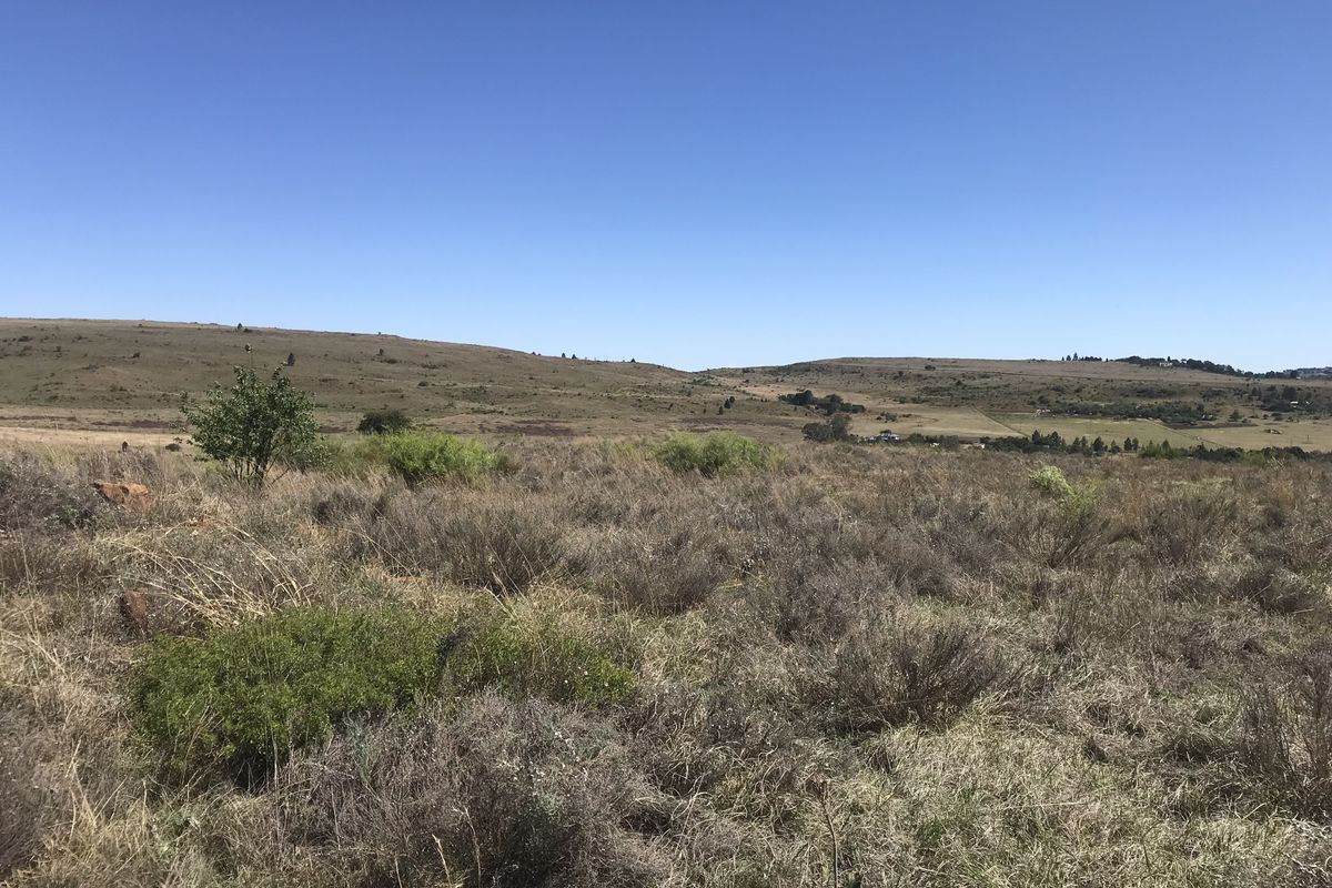 A wide-angle view of the vacant residential land, showcasing the natural landscape and surrounding hilly terrain.