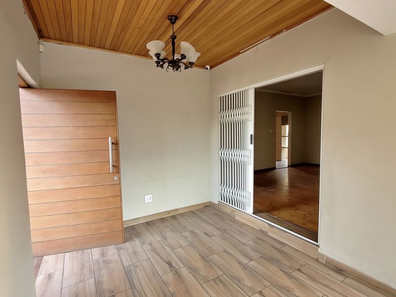 A bright entrance hall featuring a warm timber ceiling, modern wood-look floor tiles, and a secure sliding gate leading into the main living area.