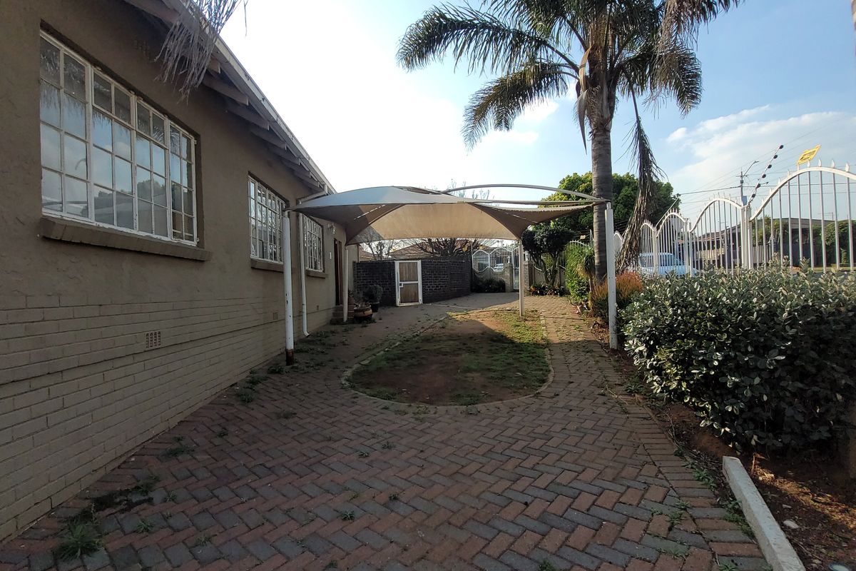 Rear exterior area featuring brick paving, a shade sail structure, and perimeter security fencing.