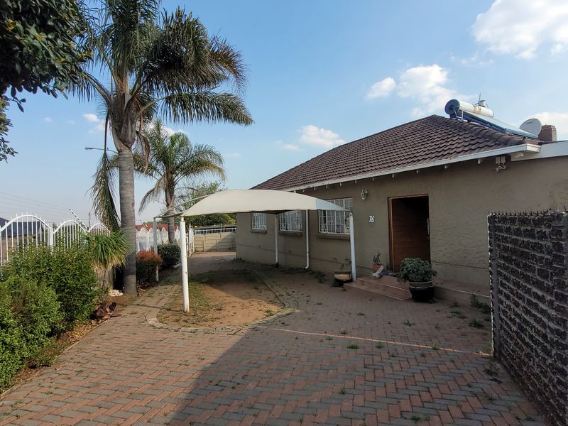 Front exterior view of the house featuring a paved driveway, shade cloth carport, solar geyser, and secure boundary walling.