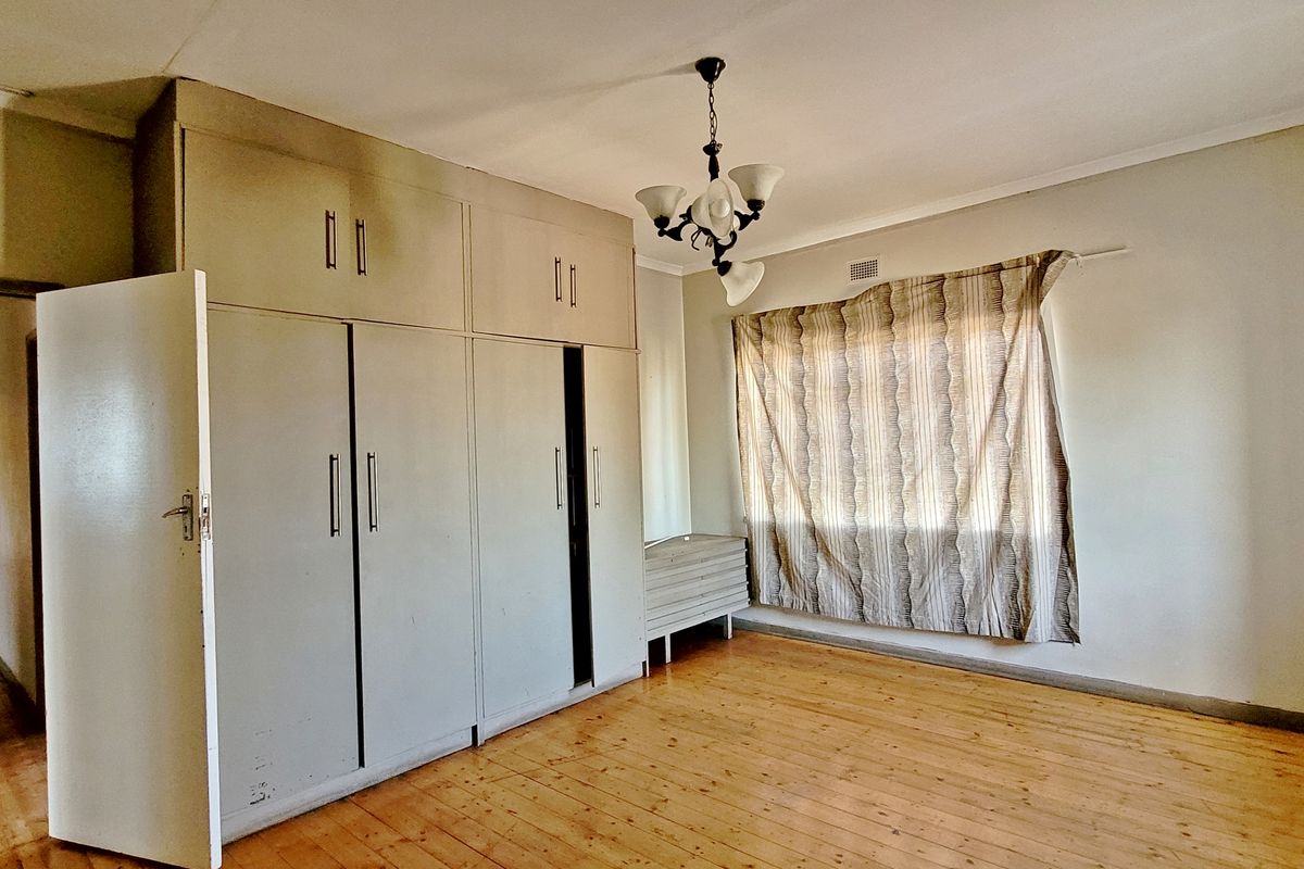 A spacious bedroom featuring original hardwood flooring and extensive built-in cupboard storage, offering a blank canvas for renovation.