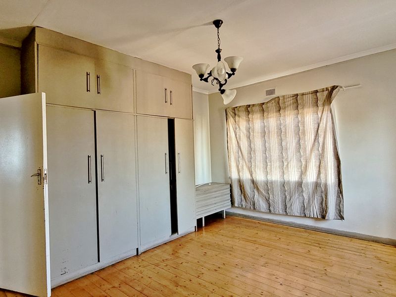 A spacious bedroom featuring original hardwood flooring and extensive built-in cupboard storage, offering a blank canvas for renovation.