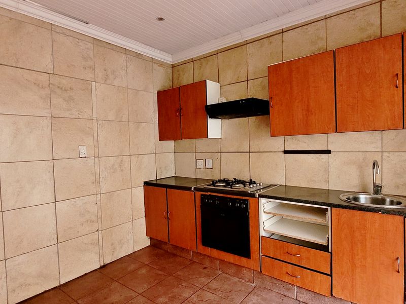 A functional kitchen featuring wooden cabinetry, a gas hob, built-in oven, extractor fan, and tiled finishes throughout.