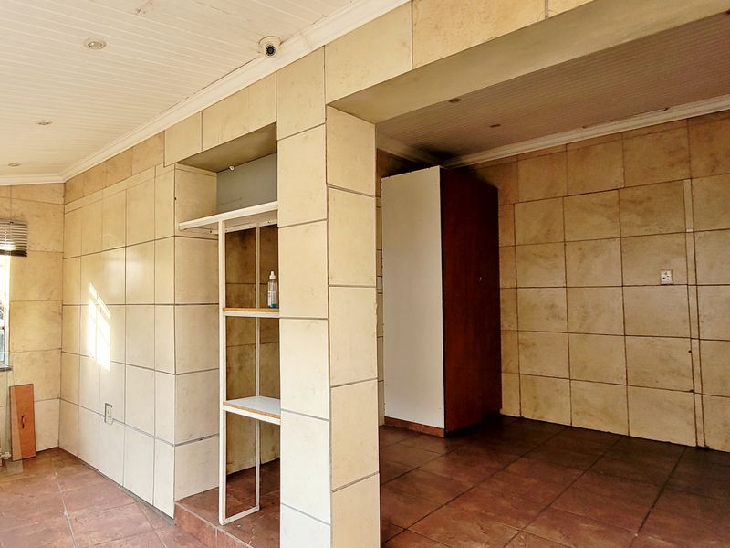 An empty living area featuring tiled walls and flooring, recessed lighting, and a built-in shelving unit, offering a blank canvas for renovation.