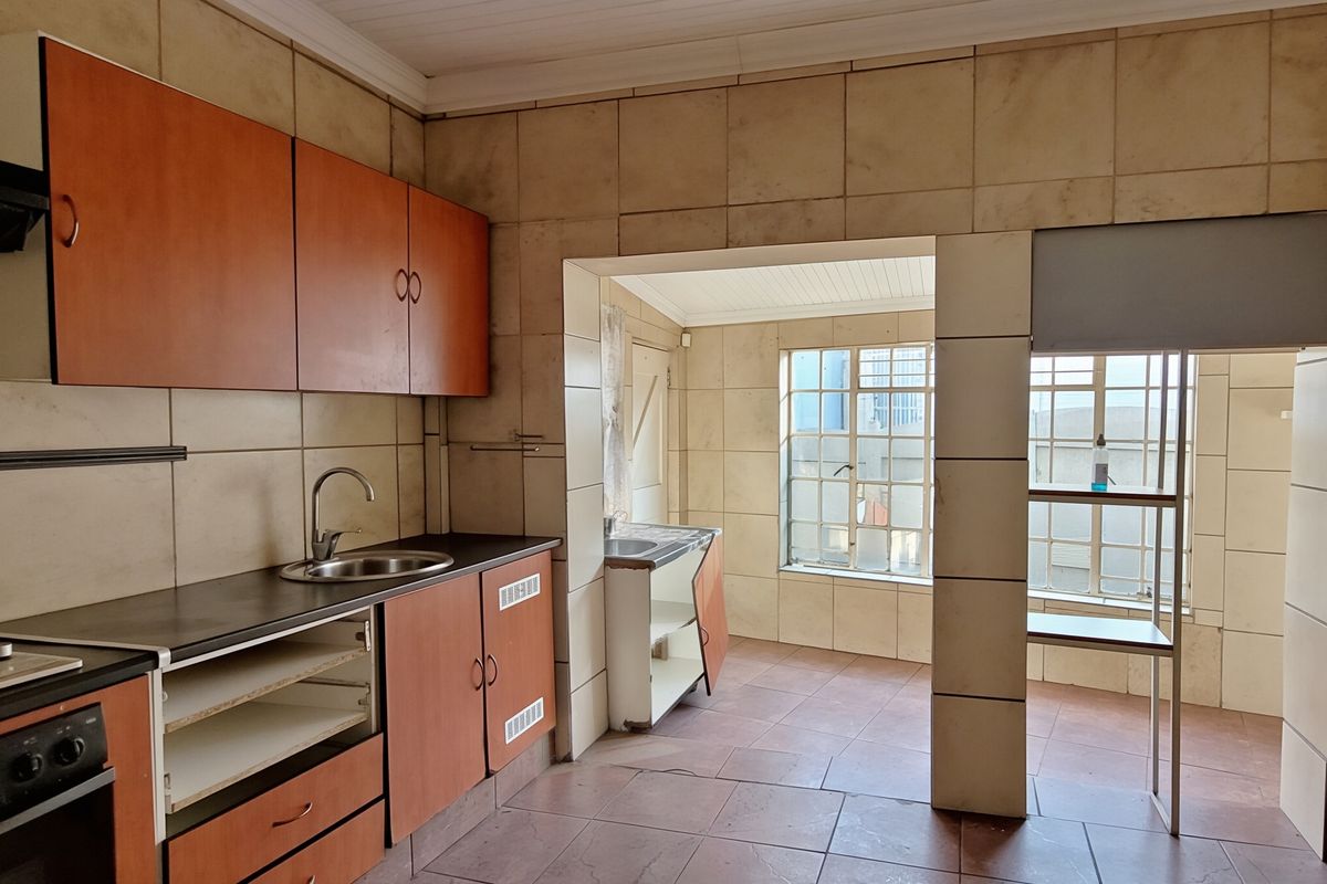 A dated kitchen featuring built-in cabinetry, tiled walls, and flooring, with an adjacent scullery area. The space requires cosmetic updates to modernize the finishes.