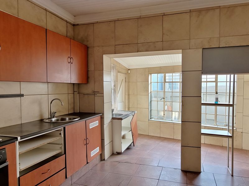 A dated kitchen featuring built-in cabinetry, tiled walls, and flooring, with an adjacent scullery area. The space requires cosmetic updates to modernize the finishes.