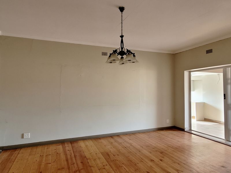 An empty living room featuring polished hardwood flooring, a central chandelier, and a sliding glass door leading to an adjacent space.