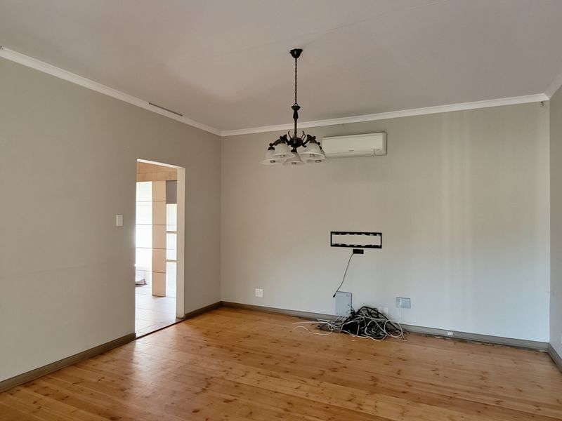 A spacious, empty living room featuring polished timber flooring, a wall-mounted air conditioning unit, and a central ceiling light fixture.