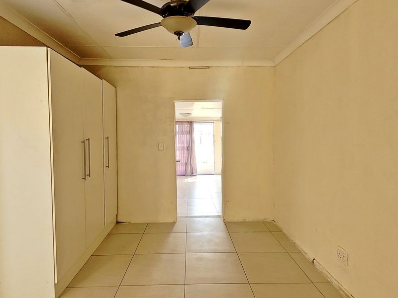 An empty bedroom featuring built-in cupboards, tiled flooring, and a ceiling fan, requiring minor cosmetic updates to the walls and skirting.