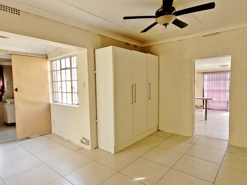 A bedroom featuring tiled flooring, a built-in wardrobe, and a ceiling fan, with access to adjacent living areas.