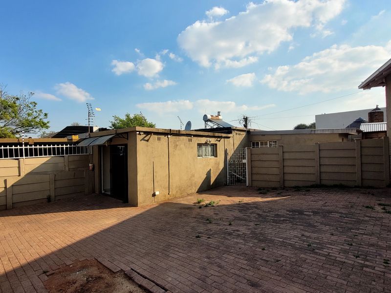Rear exterior view of the cottage featuring a paved courtyard, precast boundary walls, and a solar water heating system on the roof.