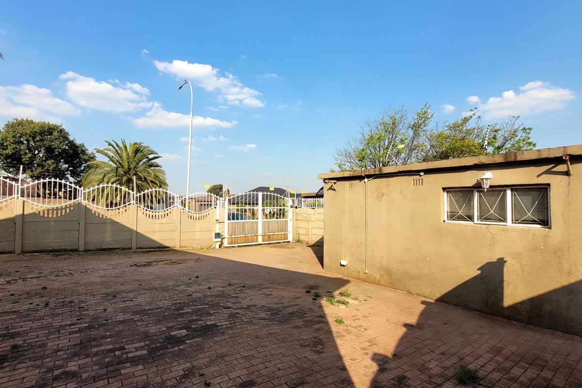 A paved rear courtyard area featuring a perimeter wall with security fencing and a gated entrance, providing a functional outdoor space.
