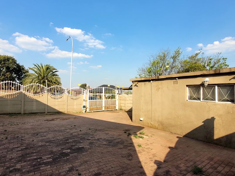 A paved rear courtyard area featuring a perimeter wall with security fencing and a gated entrance, providing a functional outdoor space.