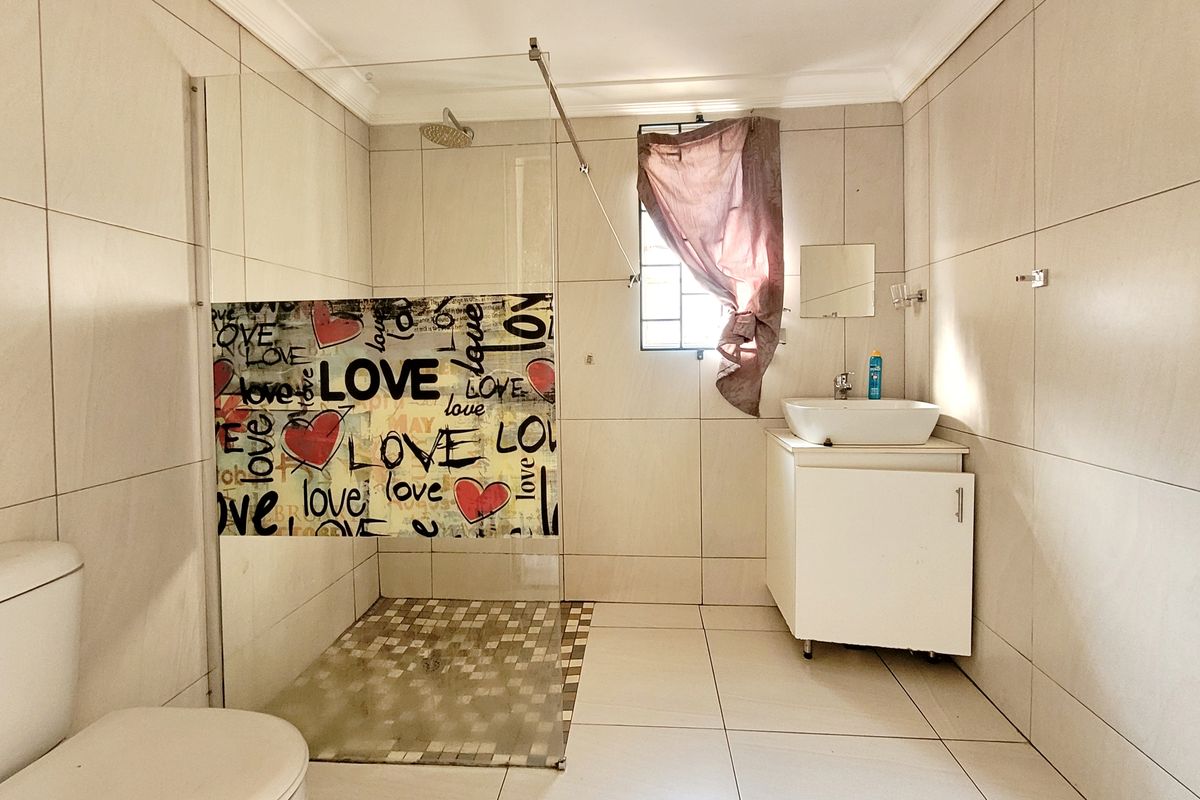 A functional bathroom featuring a glass-enclosed shower, vessel sink vanity, and neutral wall tiling. The space is well-lit with a window for natural ventilation.