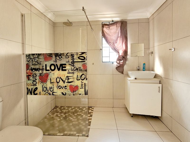 A functional bathroom featuring a glass-enclosed shower, vessel sink vanity, and neutral wall tiling. The space is well-lit with a window for natural ventilation.