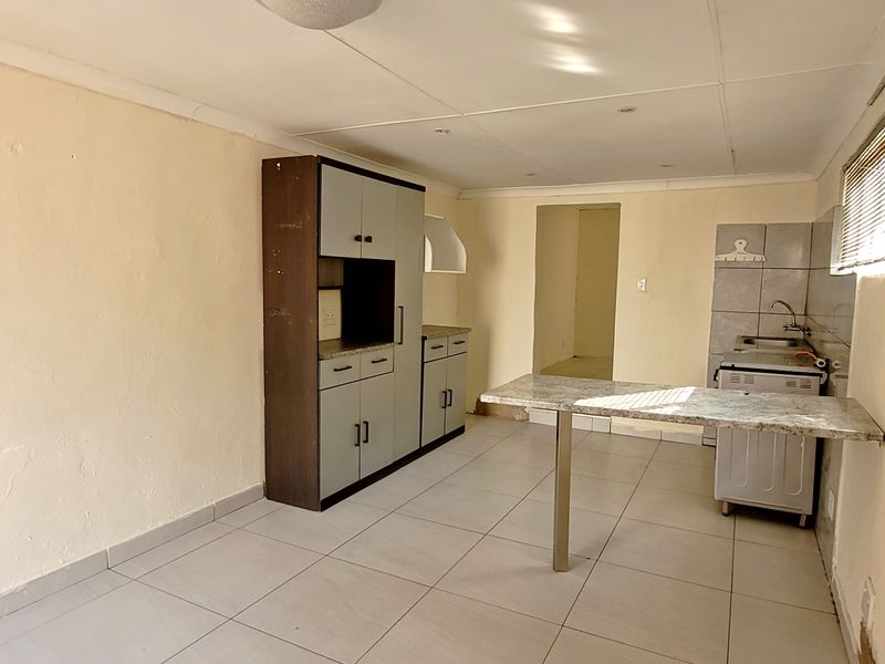 A compact, empty kitchen featuring tiled flooring, built-in cabinetry, and a stone breakfast bar, offering a functional space ready for modernization.
