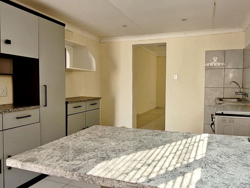 A functional kitchen featuring built-in cabinetry, laminate countertops, and a tiled backsplash, offering a clean and practical space ready for personalization.