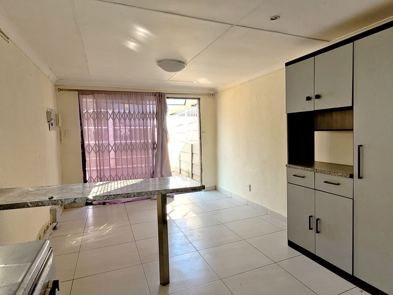 A functional kitchen area featuring built-in cabinetry, tiled flooring, and direct access to the exterior through a sliding door with a security gate.