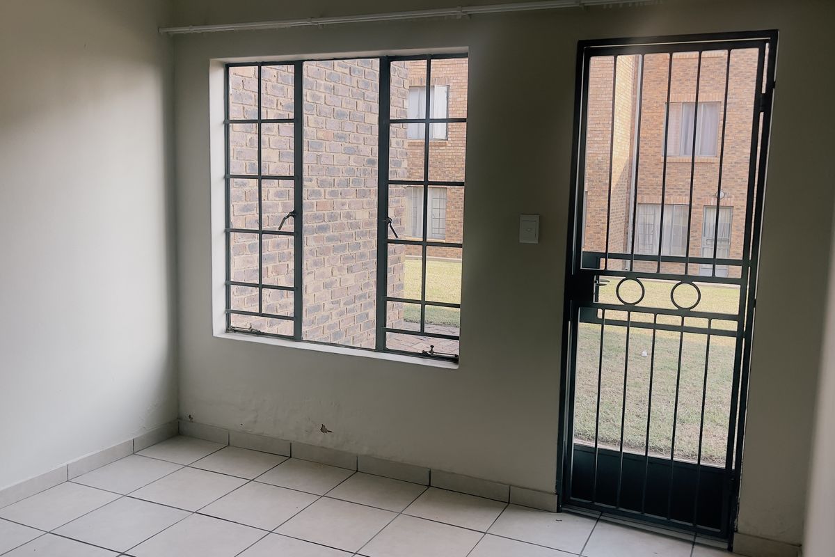 An empty living area featuring tiled flooring, steel-framed windows, and a secure metal entrance gate, offering a blank canvas for personalization.