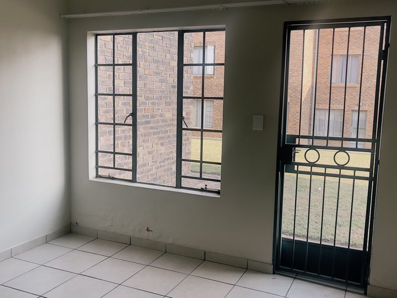An empty living area featuring tiled flooring, steel-framed windows, and a secure metal entrance gate, offering a blank canvas for personalization.