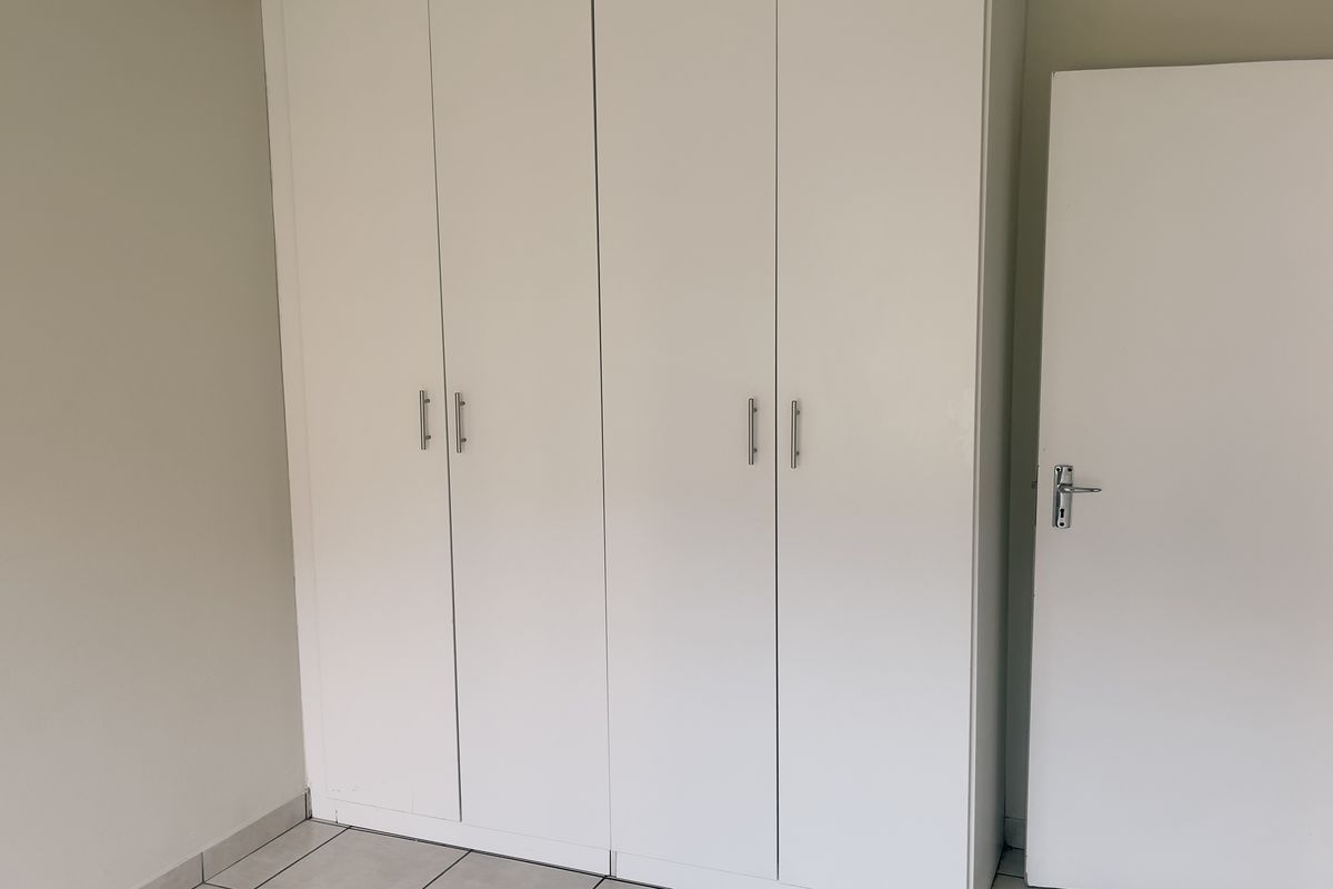 A clean, empty bedroom featuring white built-in cupboards and neutral tiled flooring, providing a blank canvas for personalization.