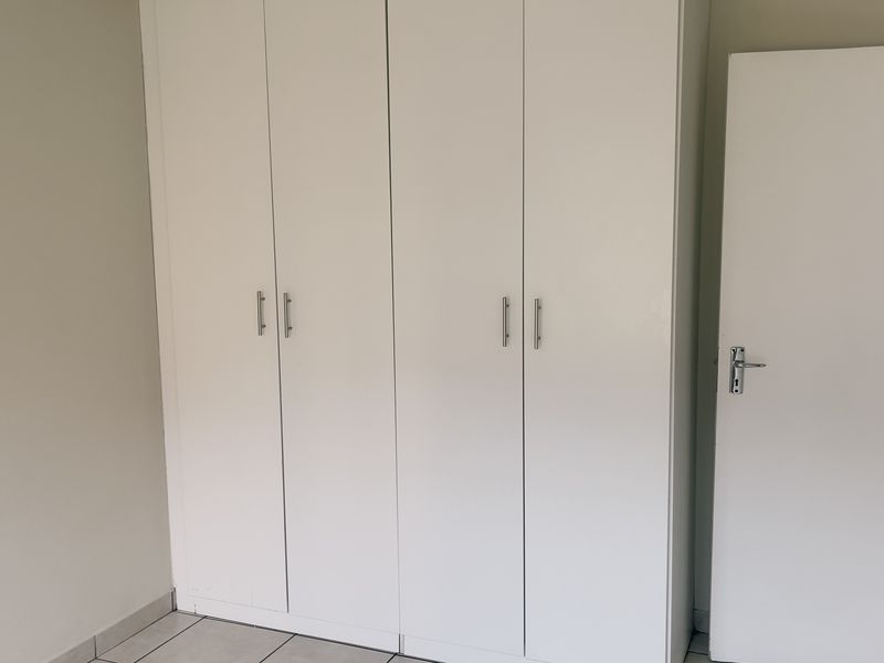 A clean, empty bedroom featuring white built-in cupboards and neutral tiled flooring, providing a blank canvas for personalization.