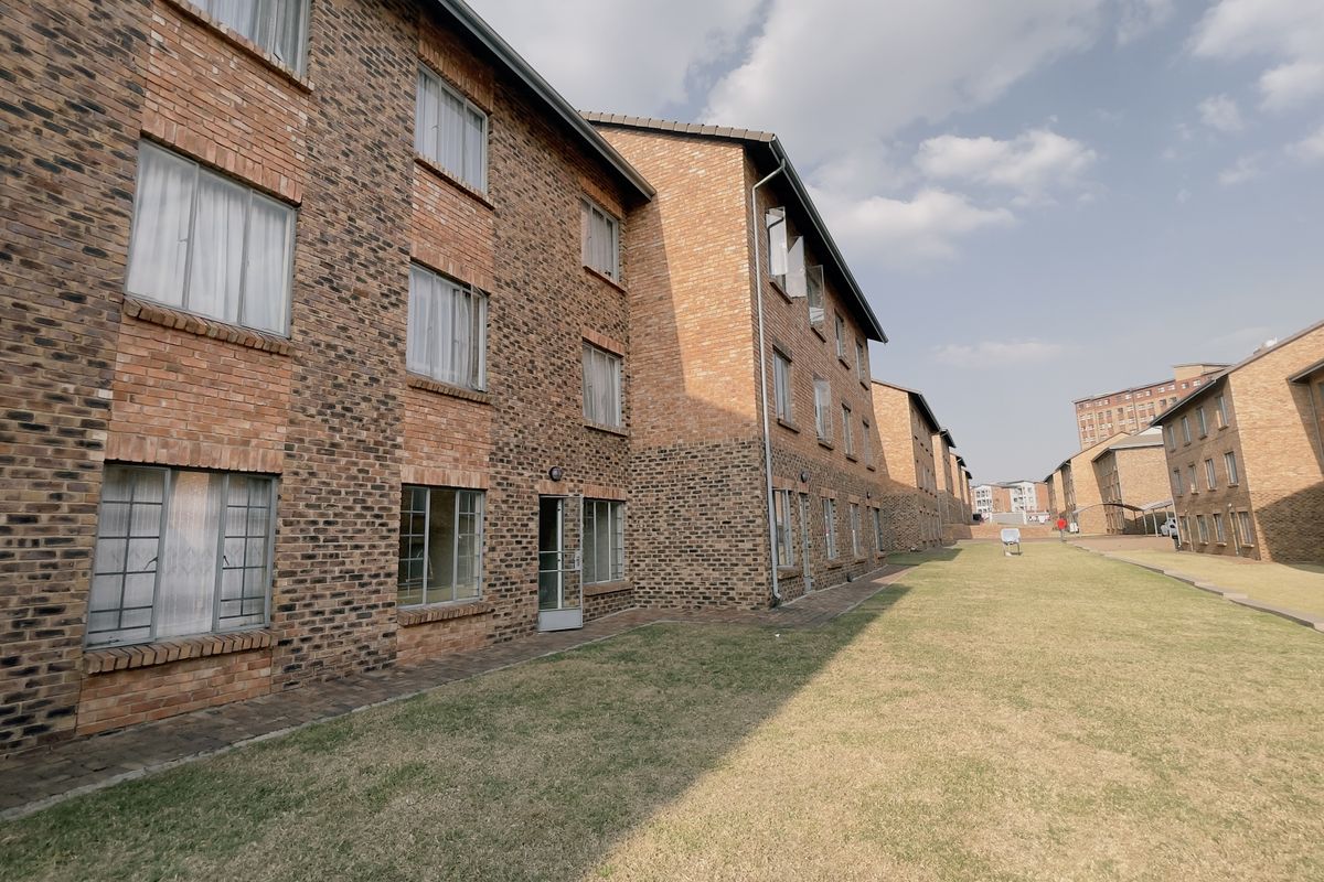 Exterior view of a multi-story apartment complex featuring face brick construction, aluminium window frames, and a shared lawn area.