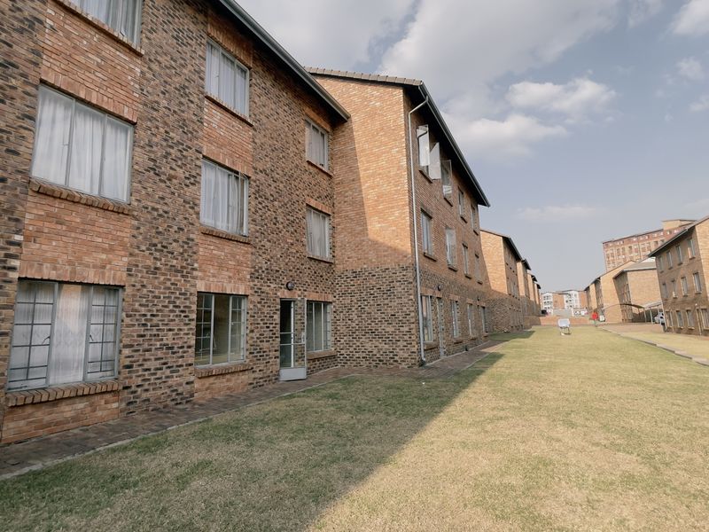 Exterior view of a multi-story apartment complex featuring face brick construction, aluminium window frames, and a shared lawn area.