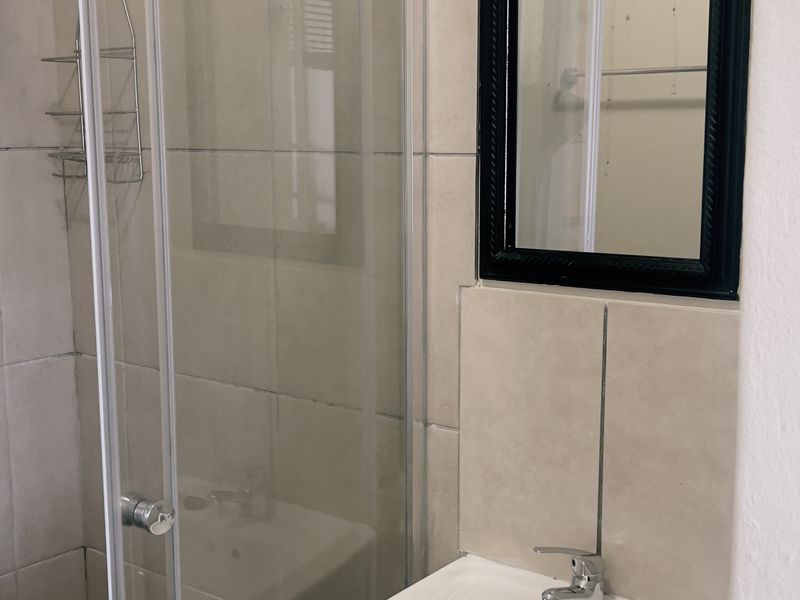 A functional bathroom featuring a pedestal basin with a chrome mixer tap and a glass-enclosed shower with tiled finishes.