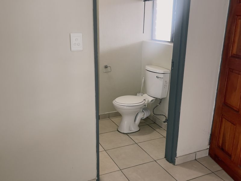 A functional, compact bathroom featuring tiled flooring, a standard toilet, and a louver window for ventilation.