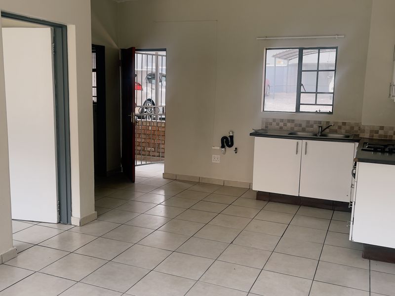Open-plan kitchen and living area featuring tiled flooring, built-in cabinetry, a gas hob, and direct access to an exterior security gate.