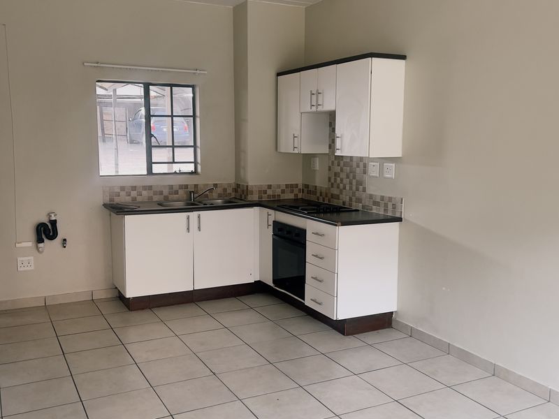 A functional, empty kitchen featuring white cabinetry, built-in oven and hob, tiled backsplash, and neutral tiled flooring.