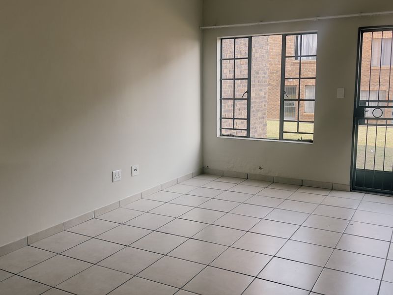 An empty living area featuring neutral tiled flooring, a security gate, and large windows with security bars, offering a blank canvas for interior design.