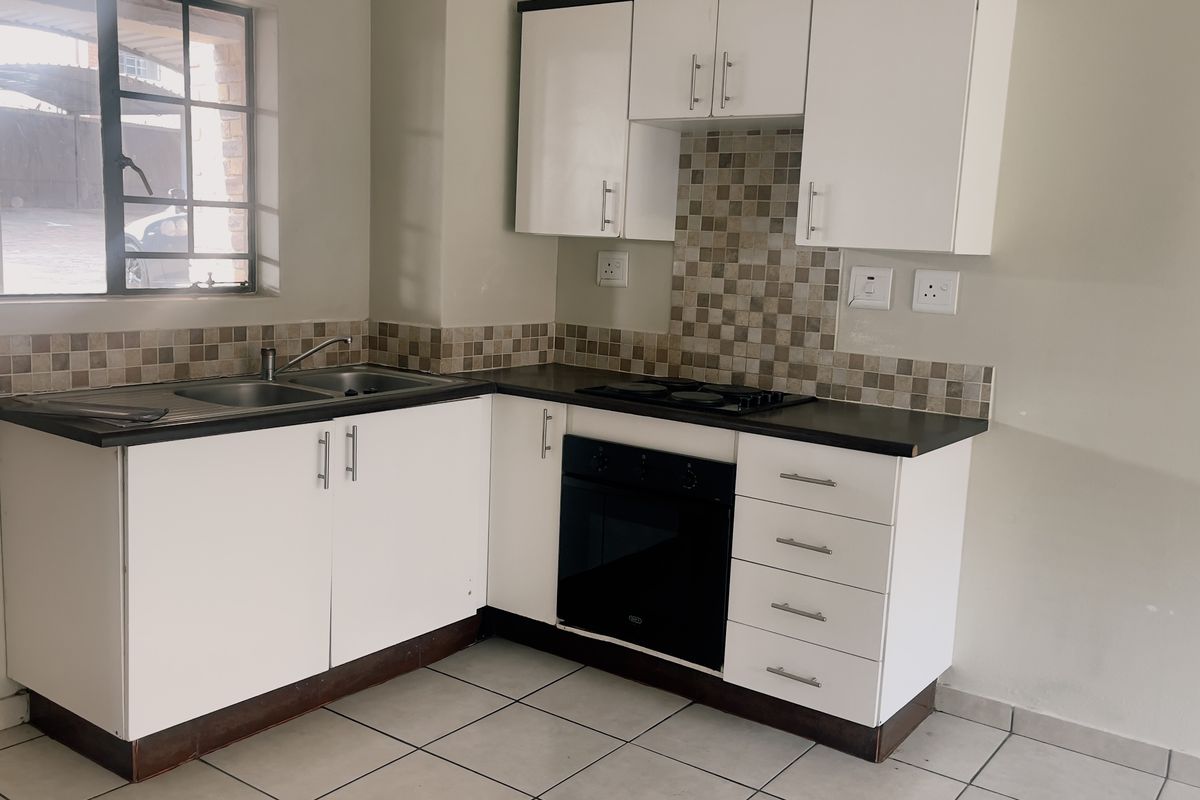 A functional kitchen featuring white cabinetry, dark countertops, a mosaic tile backsplash, and built-in oven and hob, set against neutral walls and tiled flooring.