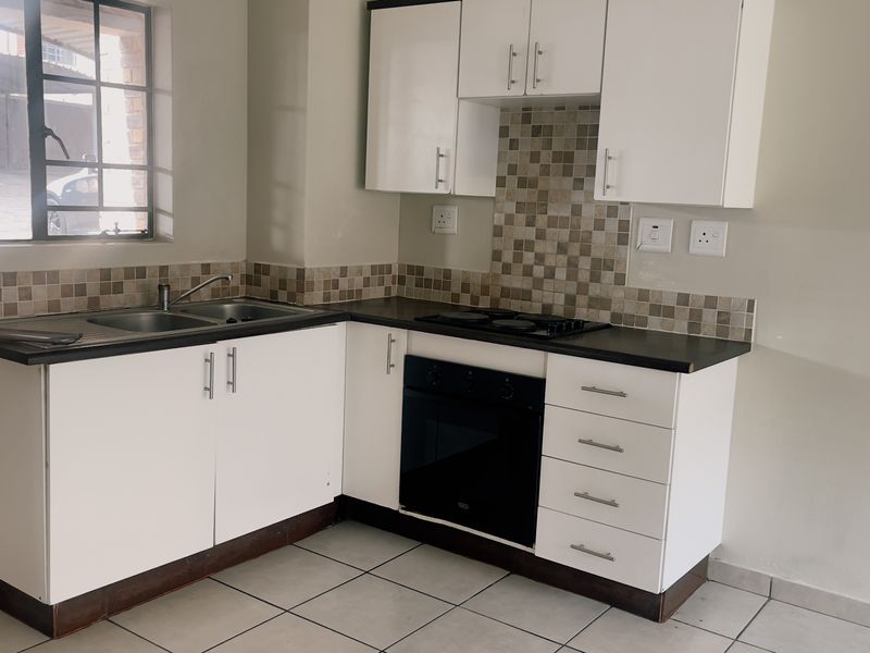 A functional kitchen featuring white cabinetry, dark countertops, a mosaic tile backsplash, and built-in oven and hob, set against neutral walls and tiled flooring.