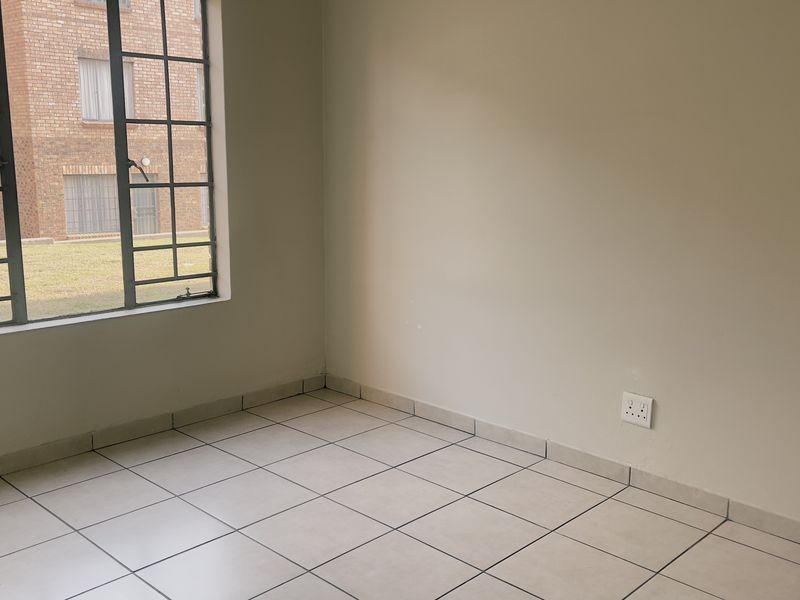 A vacant bedroom featuring neutral tiled flooring, a steel-framed window, and a standard electrical wall socket.