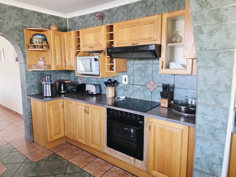 A functional kitchen featuring traditional wooden cabinetry, dark laminate countertops, an electric hob, and a built-in oven, framed by a distinctive tiled archway.