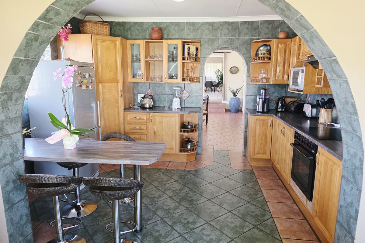 A traditional kitchen featuring wooden cabinetry, dark laminate countertops, tiled flooring, and a distinctive arched entryway leading to the adjacent living space.