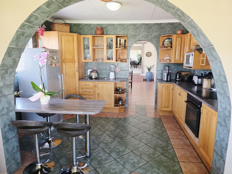 A traditional kitchen featuring wooden cabinetry, dark laminate countertops, tiled flooring, and a distinctive arched entryway leading to the adjacent living space.