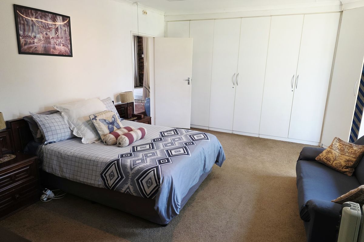 A spacious bedroom featuring extensive built-in cupboards and carpeted flooring, offering ample storage and a comfortable layout.