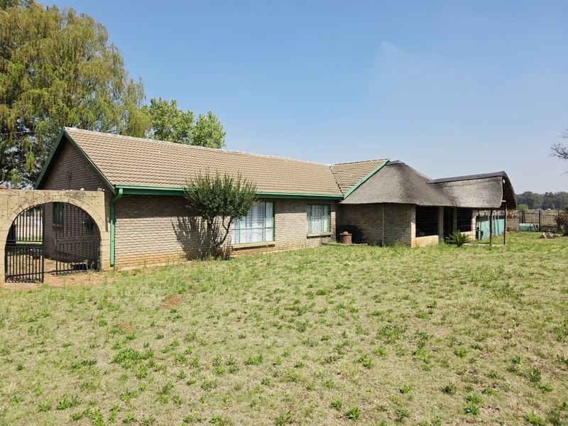 Rear view of a facebrick small holding dwelling featuring a combination of tiled and thatched roofing with an attached covered patio area.