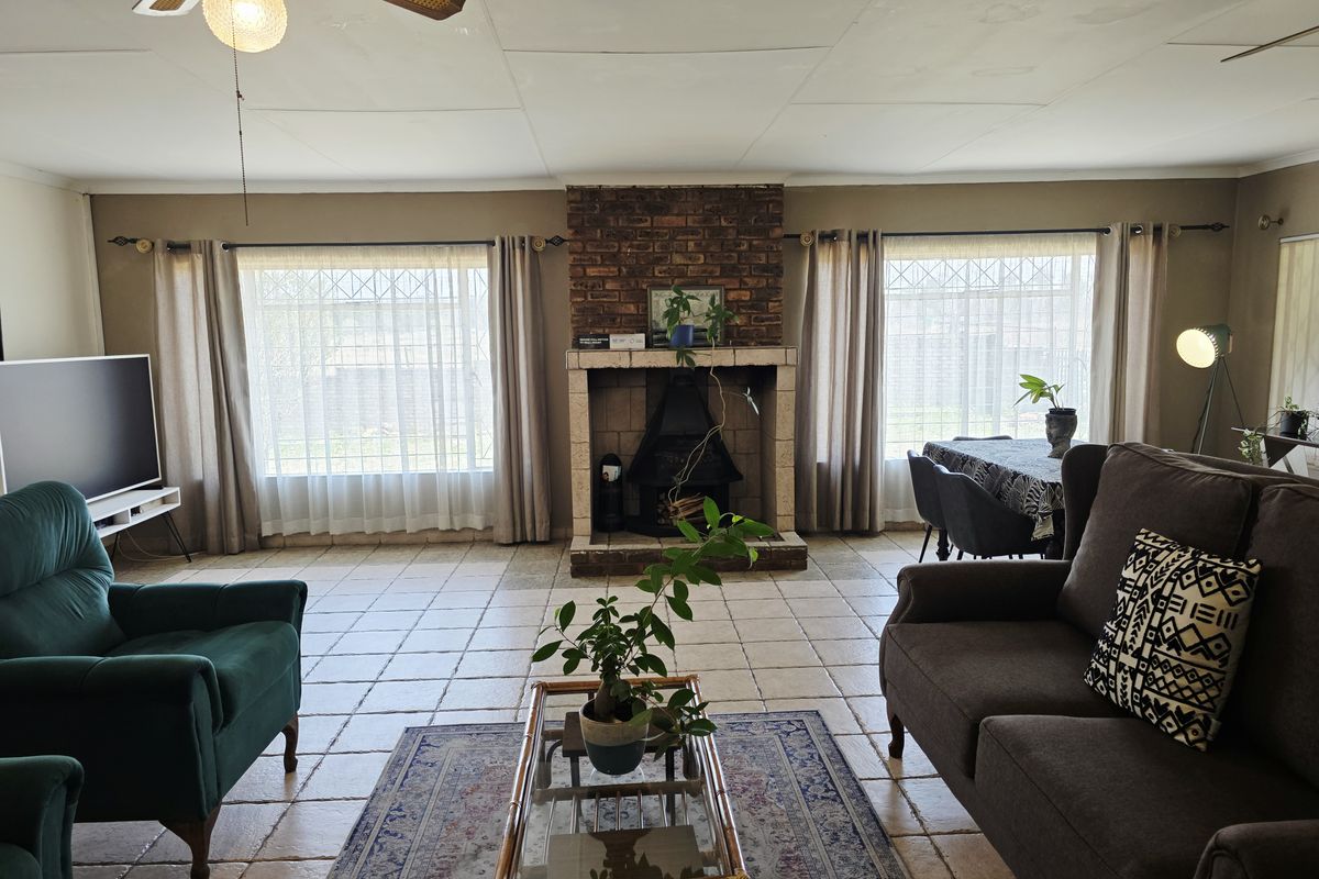 Spacious living room featuring a central brick fireplace, tiled flooring, and large windows providing ample natural light.