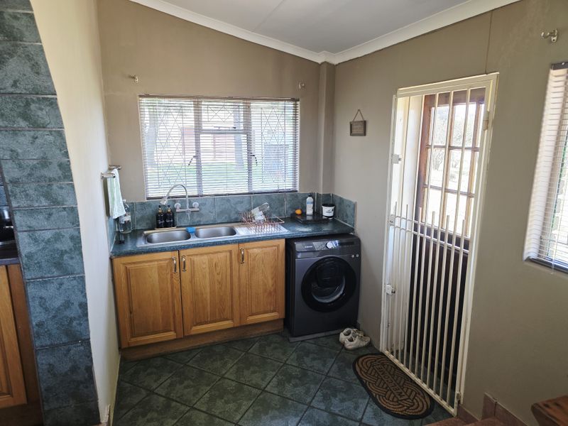 Functional laundry area featuring built-in cabinetry, a double basin sink, tiled splashbacks, and direct access to the exterior via a security gate.